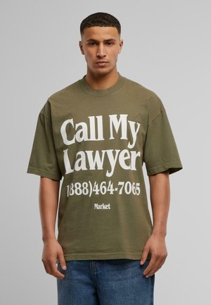 Oliven grøn bomulds t-shirt med oversized pasform. Fronten har stor hvid tekst med teksten "Ring til min advokat" og et telefonnummer.