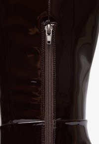 Bottes noires brillantes jusqu'au genou avec un design élégant, une fermeture éclair sur le côté avec des accessoires en argent et une texture lisse.