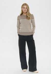Maglione a righe beige e crema con colletto tondo, fondo a coste e maniche lunghe, abbinato a pantaloni neri a gamba larga a vita alta e scarpe chiare.