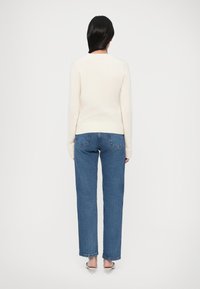 Kreemivärviline kampsun soonikkoes ääre ja varrukatega, kombineeritud siniste sirge säärtega teksadega. Sile tekstuur ja lihtne disain.