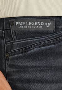 Tamno plave traperice s istaknutom oznakom "PME LEGEND AMERICAN CLASSIC." Imaju prednju džepu s kontrastnim šavovima.