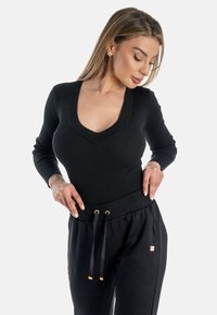 Top negro de manga larga con diseño de escote en V, combinado con pantalones negros con cordón y detalles en tono dorado.