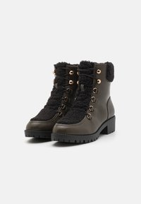 Bottines vert foncé avec un dessus en polaire noire texturée, œillets dorés, design à lacets et semelle épaisse en caoutchouc noir.