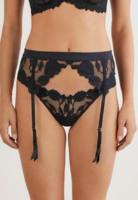 Schwarzer Spitze-Gürtel mit floralen Mustern, ausgestattet mit einem breiten Taillenbund, transparenter Netzstruktur und verstellbaren Trägern mit Bandakzenten.