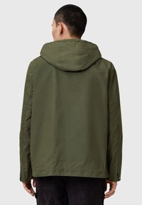 Veste à capuche vert olive avec une texture légère et lisse, présentant une coupe décontractée et des poignets à bouton-pression.