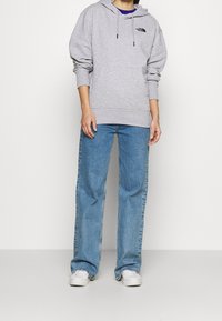 Šedá bavlněná mikina s klokankou a černým logem, v kombinaci s modrými rovnými džíny a bílými teniskami. Jednoduchý design a pohodlný střih.