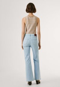 Lichtblauwe uitlopende jeans met achterzakken en een bruine label. De top is een beige mouwloze brei met gestructureerde gestreepte patronen.
