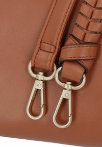 Sac en cuir brun avec une bandoulière tressée, doté de quincaillerie en métal doré et de fermoirs à pince en forme de homard, mettant en valeur la texture et les détails.