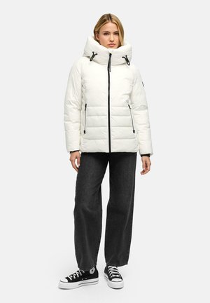 Woman wearing a white puffer jacket with a high collar, black wide-leg jeans, and black high-top sneakers standing against a plain light background.