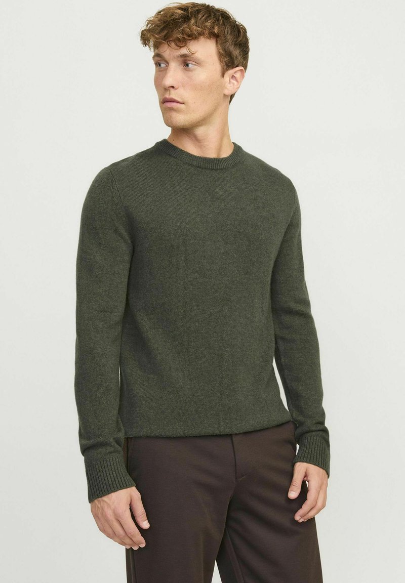 Suéter de punto de color verde oscuro con cuello redondo y puños acanalados, combinado con pantalones oscuros. La textura parece suave y acogedora.