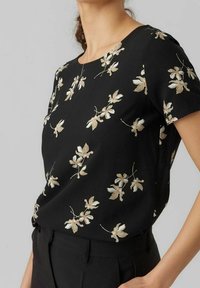 Top negro de manga corta con un patrón floral en crema claro y verde. Tejido suave con un corte relajado y escote redondo.