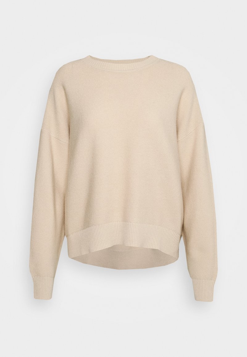 Beige stickad tröja med ribbat fåll och ärmslut, vida ärmar och en något kortad silhuett. Mjuk textur och avslappnad passform.