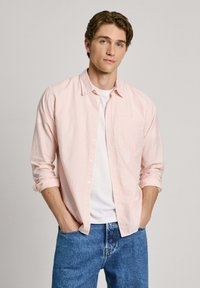 Svetloružová a biela pruhovaná košeľa na gombíky, s jednou náprsníkou. Nosená cez biely tričko a modré denimové džínsy.