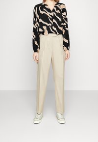 Blusa a maniche lunghe nera e beige con motivo, abbinata a pantaloni beige a vita alta e sneakers di colore chiaro.