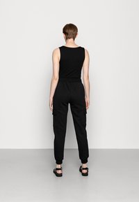 Svart ärmlös topp kombinerad med svarta cargo-byxor med fickor och uppvikta benslut. Modellen bär svarta sandaler. Neutral bakgrund.