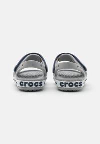 Infradito Crocs grigi con una fascia blu scuro, suola bianca e marchio "crocs" sul tallone, dotati di una soletta perforata e design aperto sul retro.