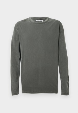 Ilgi piedurkņu, apaļās izgriezuma krekls izbalējušā tumši pelēkā krāsā ar redzamām šuvēm apkaklē, piedurkņu galos un apakšmalā, uz balta fona.