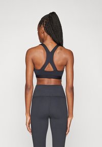 Soutien-gorge de sport noir avec un design dos nageur et des bretelles larges ; associé à un legging noir taille haute. Texture lisse, détails minimaux.