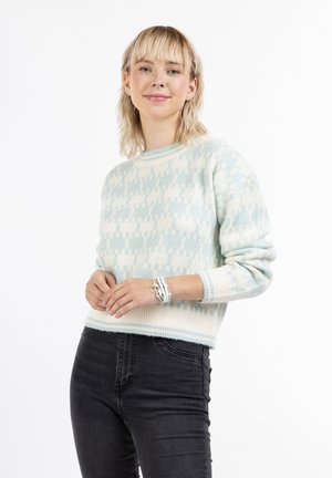 Világoskék és krém színű mintás kötött pulóver, kerek nyakkal és bordás mandzsettával, fekete farmerral és rétegezett karkötőkkel párosítva.