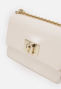 Bežová kožená kabelka se zlatým řetízkovým popruhem, obdélníkového tvaru, s texturovaným povrchem a výrazným zlatým zámkem na přední straně.