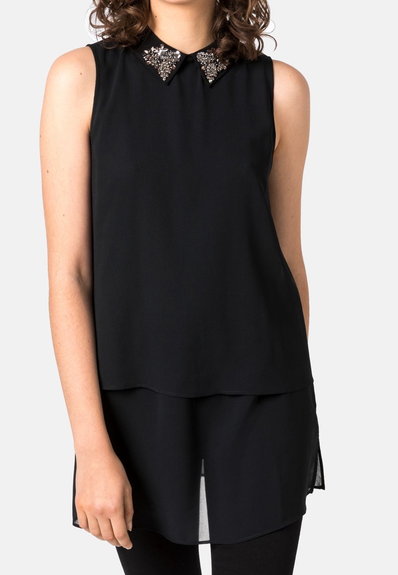 Top sans manches noir à coupe ample, col orné de sequins géométriques et ourlet superposé pour plus de longueur.