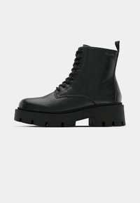 Stivale alla caviglia in pelle nera con suola in gomma spessa e testurizzata, punta rotonda e occhielli in metallo per i lacci. Presenta un tappo di trazione sul retro.