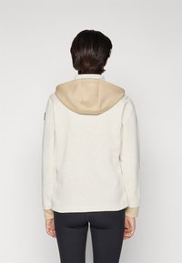 Hooded sweatshirt in cream with a textured finish and beige hood. Features fitted cuffs and a relaxed silhouette. Plain design with no visible logos.