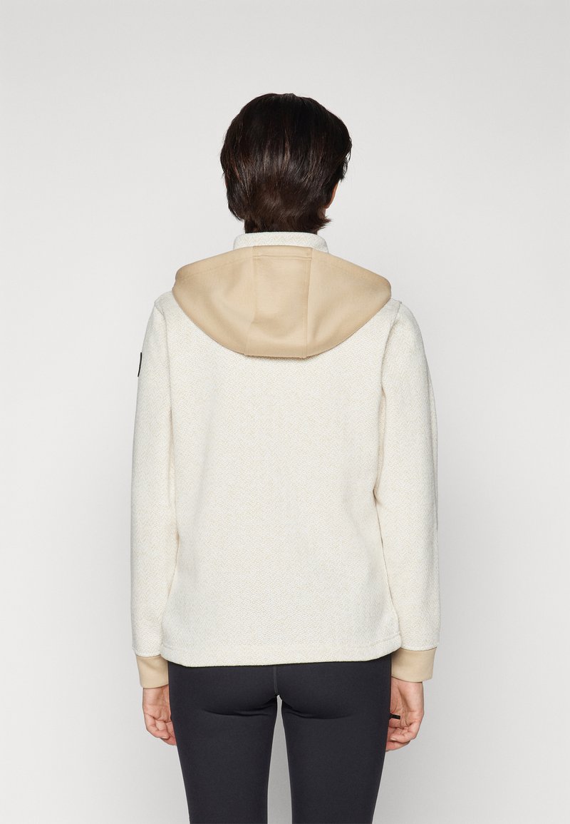 Sweat à capuche crème avec une finition texturée et une capuche beige. Présente des poignets ajustés et une silhouette décontractée. Design uni sans logos visibles.