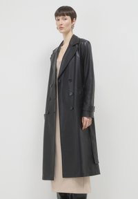 Pelliccia nera in pelle doppiopetto con ampi revers, tasche laterali e una linea lunga e dritta. Texture liscia e lucida.