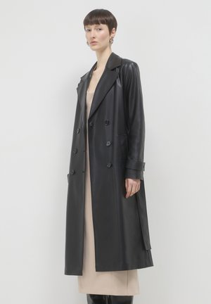 Pelliccia nera in pelle doppiopetto con ampi revers, tasche laterali e una linea lunga e dritta. Texture liscia e lucida.