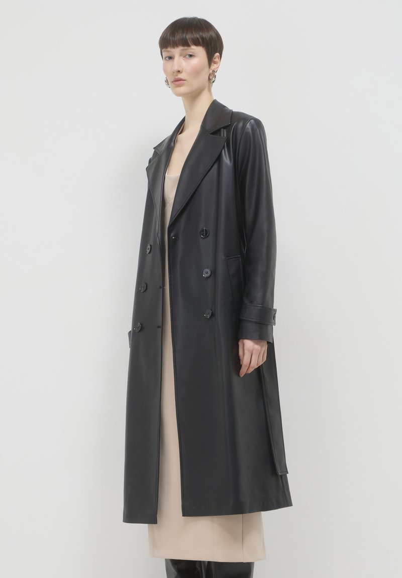 Pelliccia nera in pelle doppiopetto con ampi revers, tasche laterali e una linea lunga e dritta. Texture liscia e lucida.