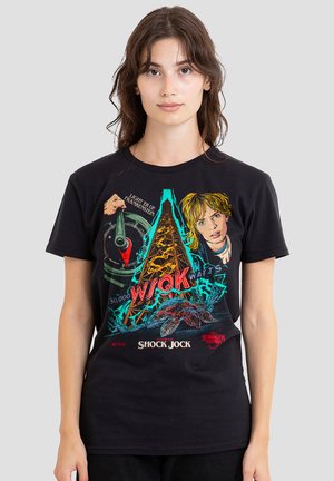 Young woman wearing black Stranger Things "Shock Jock" graphic t-shirt featuring character, radio dial, and creature illustration.