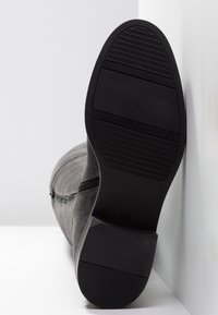 Gray suede ankle boot with a black rubber sole, featuring a textured pattern, reinforced heel, and a side zipper for easy wear.