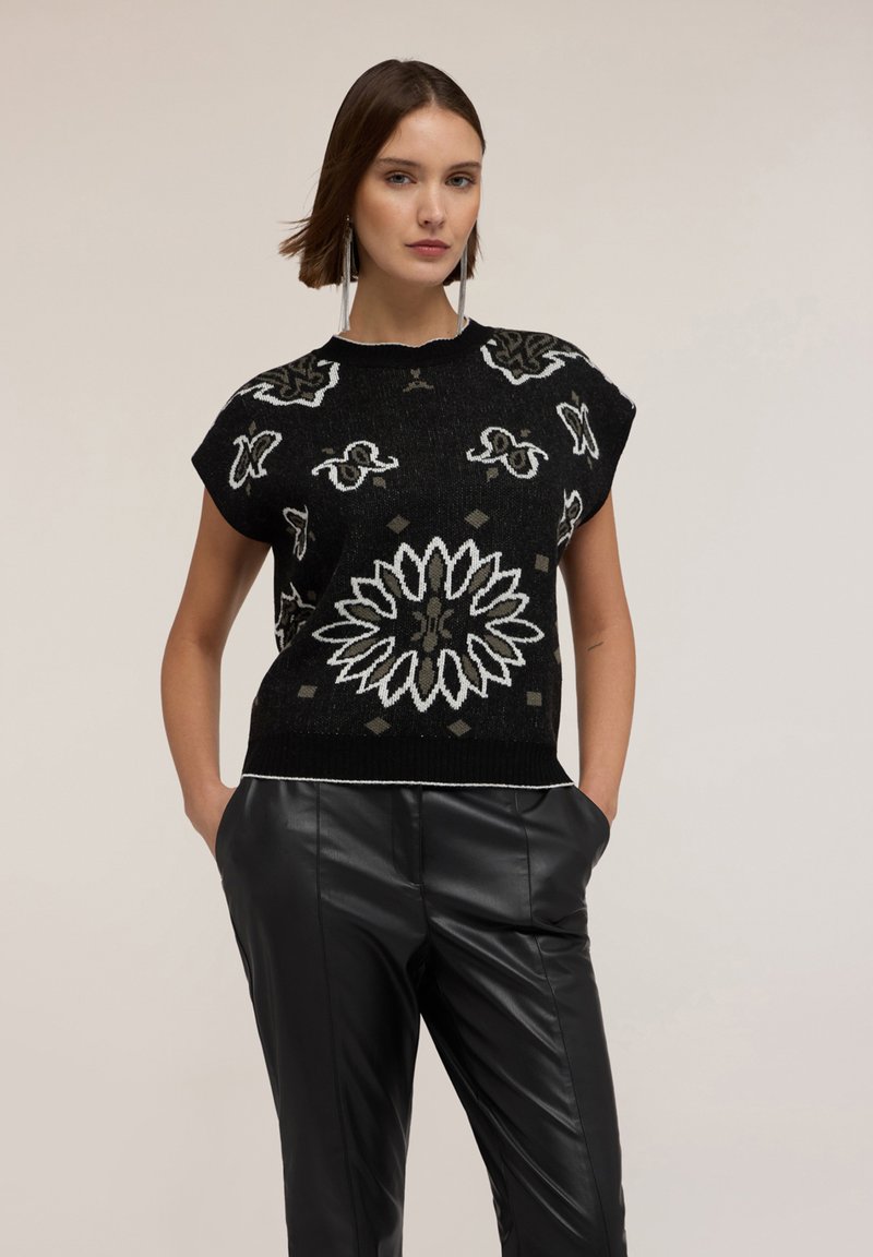 Suéter negro de punto con mangas cortas, que presenta intrincados patrones florales en blanco y gris, acompañado de unos elegantes pantalones de cuero negros.