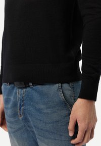 Pull en tricot noir avec un ourlet côtelé, porté avec un jean denim bleu clair. Le tissu semble doux et texturé, avec une coupe ajustée.