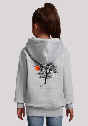 Kind mit braunem Pferdeschwanz trägt einen grauen Kapuzenpullover mit einem schwarzen Baum, einer orangefarbenen Sonne und fliegenden Vögeln sowie dem Wort "Escape" auf dem Rücken.