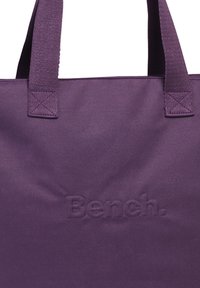 Paarse stoffen draagtas met geborduurd "Bench." logo. Stevige stof, brede handvatten en een eenvoudig, rechthoekig ontwerp. Soepele textuur.