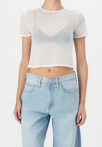 Top blanco transparente de manga corta con un diseño corto. Combinado con unos vaqueros holgados de lavado claro, con cierre de botón y bolsillos.