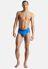 Blå simbyxor med en slät yta, med en enfärgad design och svarta accentlinjer på midjan. Utformade för en tät passform.