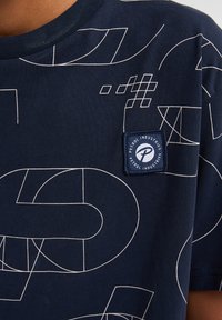 Camiseta de algodón de color azul marino con patrones geométricos abstractos en blanco y un parche de la marca en un cuadrado en el lado izquierdo del pecho.