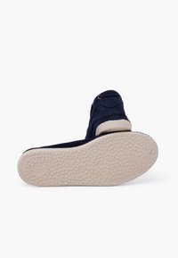 Navy canvas shoe with a textured rubber sole, rounded toe, and two gold eyelets. The sole is light beige with a patterned tread.