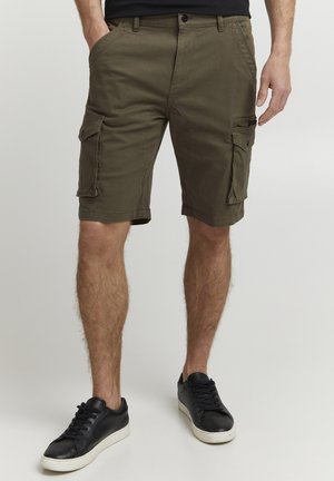 Shorts cargo vert olive avec poches latérales, fermeture par bouton, devant plat et tissu légèrement texturé. Associés à des baskets noires.