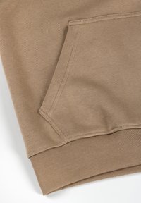 Beežika pusa tasku lähivaade, kus on nähtavad õmblused ja soonikkoes äär detail heledal taustal.