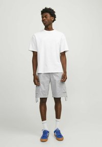 T-shirt en coton blanc, coupe ample, associé à un short cargo gris clair, doté de poches. Des baskets bleues avec des semelles en caoutchouc marron complètent le look.