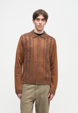 Cardigã de malha castanho com gola e fecho de botão. Apresenta um padrão geométrico castanho mais escuro na parte da frente e punhos canelados. Tecido texturizado.