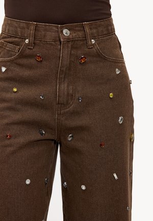 Jeans en denim marron avec une coupe droite, ornés de strass décoratifs de différentes formes et couleurs sur la surface avant.