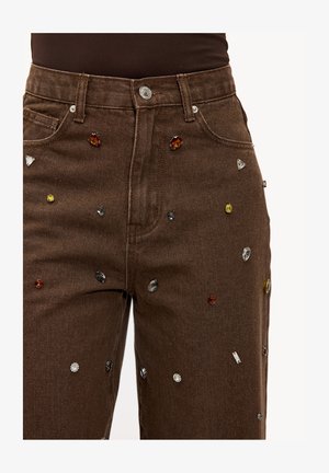 Jeans en denim marron avec une coupe droite, ornés de strass décoratifs de différentes formes et couleurs sur la surface avant.