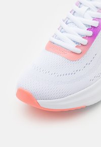 Zapatilla deportiva blanca con un tejido de punto transpirable, que presenta un acento degradado en rosa y púrpura en la parte superior, y una puntera rosa.