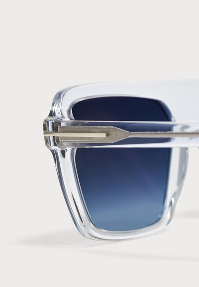 Lunettes de soleil à monture transparente claire avec verres dégradés bleu foncé et branches en métal argenté, vues en gros plan de face.