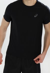 Camiseta atlética negra hecha de tela que absorbe la humedad. Cuenta con un cuello redondo y un sutil logotipo gris en el lado izquierdo del pecho. Mangas cortas.